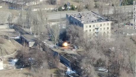 Ten zrzut ekranu z materiału z drona przedstawia pojazd wojskowy strzelający w pobliżu budynku.