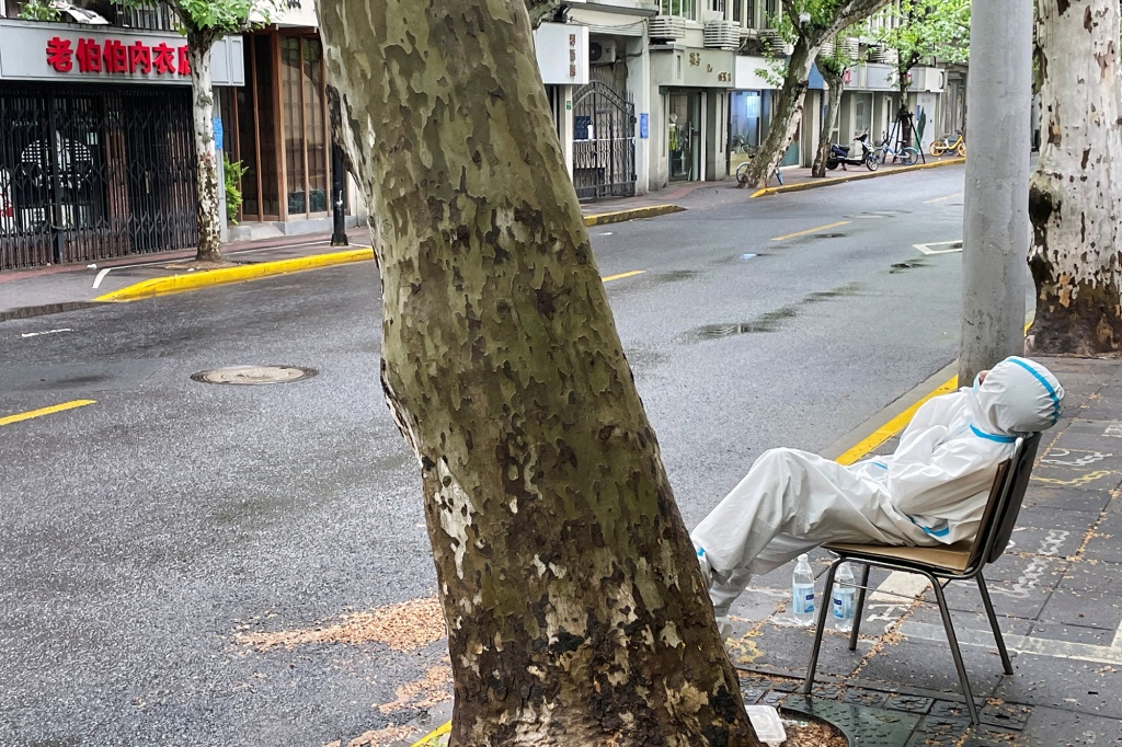 Zmęczony pracownik medyczny siedzi na pustej ulicy w Szanghaju w Chinach.