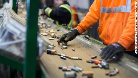 Pracownicy sortują akumulatory, które poruszają się wzdłuż przenośnika taśmowego w zakładzie recyklingu.