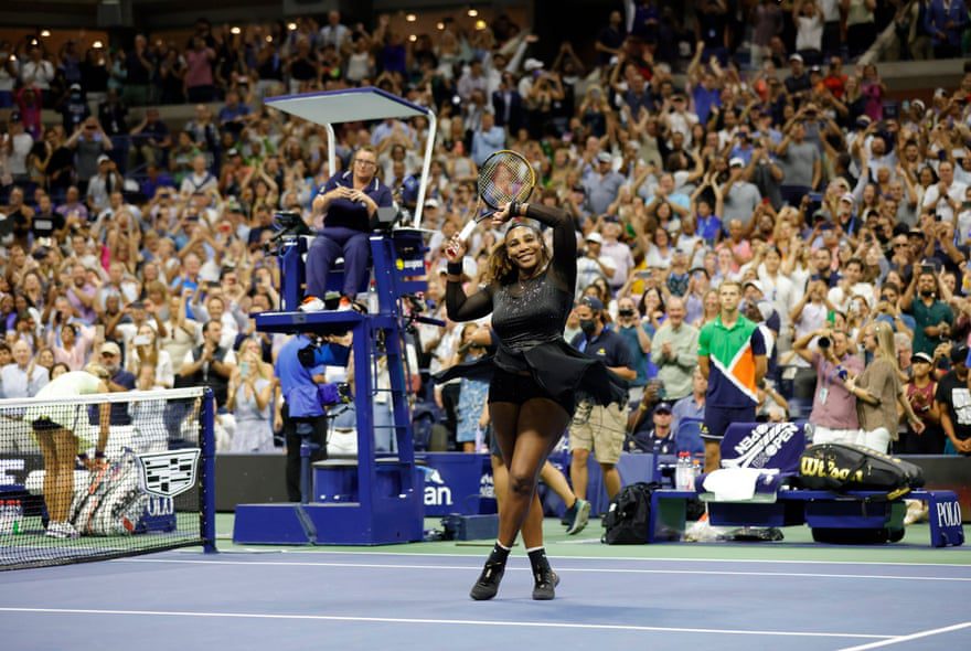 Serena Williams unosi rakietę i ramię do tłumu, stojąc na boisku po zwycięstwie