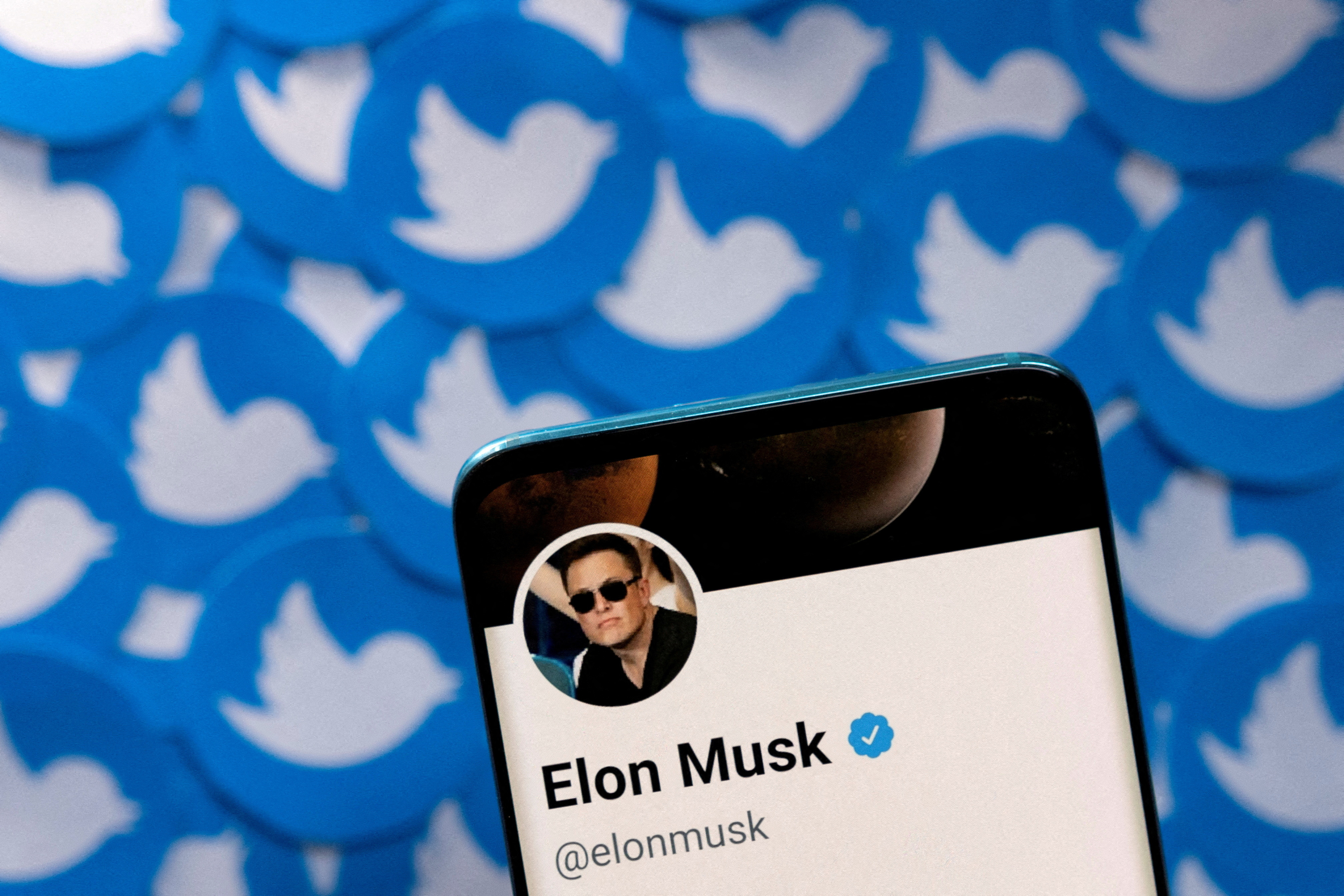 Ilustracja przedstawia profil Elona Muska na Twitterze na smartfonie i nadrukowane logo Twittera